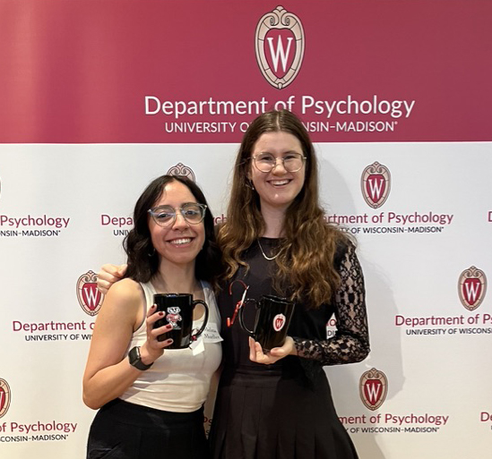 Image of Melina and Zoe holding UW-Madison mugs in front of a Department of Psychology sign